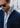 A man in sunglasses wears a blue Dolomite Double Face Overshirt, crafted with premium European craftsmanship, layered over a light blue shirt with blue buttons. He stands outdoors with a blurred building in the background.