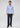 A man stands facing forward, wearing the Polish Non Iron Button Down—a business blue stripe shirt crafted from premium European cotton with a non-iron, wrinkle-resistant finish—paired with dark jeans and brown dress shoes against a plain, light gray background.