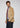 Wearing the Glasgow Velvet Stretch Sport Coat in a camel shade, a man pairs it with a light blue dress shirt, red striped tie, and dark jeans as he stands against a plain light background, gazing to his left with a neutral expression.