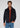 A man with wavy brown hair wears the Stockholm Corduroy Overshirt in navy, layered over a red half-zip sweater and paired with blue jeans. He stands against a plain light background, looking at the camera with a neutral expression—a refined example of versatile layering in men’s fashion.