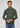 A man with short brown hair wears the Milano 1/4 Zip Merino Wool Sweater in green over a collared shirt and tie, paired with blue jeans, standing against a plain light gray background.