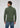 A man stands facing away, wearing a green Milano 1/4 Zip Merino Wool Sweater and blue jeans. The background is plain and light gray.