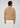A man with curly brown hair, dressed in the Milano 1/4 Zip Merino Wool Sweater in tan and white pants, stands facing away from the camera against a plain light gray background.