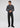 A man stands against a plain background wearing the Milano 1/4 Zip Merino Wool Sweater in dark gray, paired with black jeans and black shoes, looking slightly downward with his hands loosely clasped.