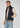 A man stands facing forward with one hand in his pocket against a plain light background, showcasing a smart business casual look that offers lightweight warmth in the dark navy Stelvio Padded Vest, styled over a beige sweater and blue jeans.
