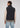 Wearing the Stelvio Padded Vest in black over a beige sweatshirt and light blue jeans, the individual stands with their back to the camera against a plain background, highlighting the vest’s lightweight warmth in a casual yet versatile style.