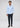 A man stands facing forward against a plain light gray background, wearing the Adams Stretch Button Down in light blue—crafted from wrinkle-resistant, stretch fabric—paired with dark slim-fit pants and brown shoes.