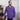A man with light skin and brown hair, dressed in the Marietta 1/4 Zip Sweater in purple and dark jeans, stands indoors beside a wooden sideboard, gazing thoughtfully into the distance.