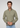 A man with wavy brown hair and stubble, wearing the Onamia Reversible 1/4 Zip in olive green as a versatile layering piece along with light blue jeans, stands against a plain light gray background, looking at the camera with a serious expression.