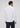 A man stands facing away, wearing the Emissary Button Down—a crisp white shirt—paired with dark jeans against a plain, light background.
