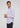 A man in the Ingalls Non Iron Button Down—a light purple shirt crafted from wrinkle-resistant cotton—paired with dark pants stands against a plain background, looking to his left with his hands gently clasped together.