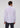 A man stands with his back to the camera, dressed in the Ingalls Non Iron Button Down—a light purple dress shirt made from wrinkle-resistant cotton—paired with dark trousers against a plain, light background.