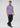 A man stands against a plain background, wearing the Lyon Reversible Polo in light purple, paired with dark jeans and navy sneakers. He looks to his left with a neutral expression and has short brown hair.