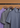 Three Lyon Reversible Polo shirts in purple, gray, and blue hang on wooden hangers against a brown background—each a men’s everyday essential designed for both style and comfort.