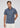 A man stands against a plain light gray background, looking forward with a neutral expression while wearing the Lyon Reversible Polo—a navy blue patterned short-sleeve shirt featuring UPF 50+ protection—paired with white pants. This men’s everyday essential blends style and functionality for any occasion.