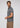 A man with short curly hair and a beard wears the Lyon Reversible Polo—a men’s everyday essential—with tan pants, standing sideways and looking off to the left against a plain light background.