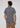 A man with curly hair, seen from behind, is wearing the men’s everyday essential— the Lyon Reversible Polo in a short-sleeve gray pattern—paired with light brown pants, standing against a plain light background.