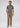 A man stands facing forward, wearing the Lyon Reversible Polo — a short-sleeve dark men’s everyday essential — paired with tan pants and beige sneakers, with one hand in his pocket against a plain light background.