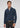 A man wearing the Milano 1/4 Zip Merino Wool Sweater—a luxury men’s sweater crafted from ultra-fine merino wool—over a light blue shirt, paired with dark pants and a beige belt, stands against a plain light gray background.
