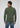 A man stands facing away, wearing a green Milano 1/4 Zip Merino Wool Sweater and blue jeans. The background is plain and light gray.