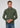 A man with short brown hair wears the Milano 1/4 Zip Merino Wool Sweater in green over a collared shirt and tie, paired with blue jeans, standing against a plain light gray background.
