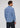 A person is standing with their back to the camera against a plain light background, wearing the Norman Button Down—an elegant European cotton plaid long-sleeve shirt in blue, white, and black—and dark jeans, exemplifying classic men’s fashion.