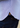 A close-up of the Panasa Stretch Button Down in a blue micro-geo pattern features its curved hem partially covering the pocket of dark blue jeans, with a small orange circular tag visible near the hem.