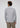 A man with curly hair is shown from behind, wearing the Ramy Button Down in light gray—crafted from premium European cotton—and khaki pants, standing against a plain white background.