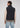 Wearing the Stelvio Padded Vest in black over a beige sweatshirt and light blue jeans, the individual stands with their back to the camera against a plain background, highlighting the vest’s lightweight warmth in a casual yet versatile style.