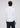 A man with curly brown hair is standing with his back to the camera, wearing the Thurnbeck Stretch Button Down—a modern white long-sleeve dress shirt—and dark pants against a plain light background.