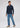 A man stands posing in a smart-casual ensemble, featuring the Zephyr Long Sleeve Stretch Polo in navy, light blue jeans, and beige sneakers against a plain light gray background. He looks to his left with one hand by his side and the other resting near his pocket.