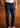 Wearing the Tailored Fit Denim jeans with a 32″ inseam, paired with a white t-shirt and white sneakers, a person stands before a wooden wall, their lower half visible.